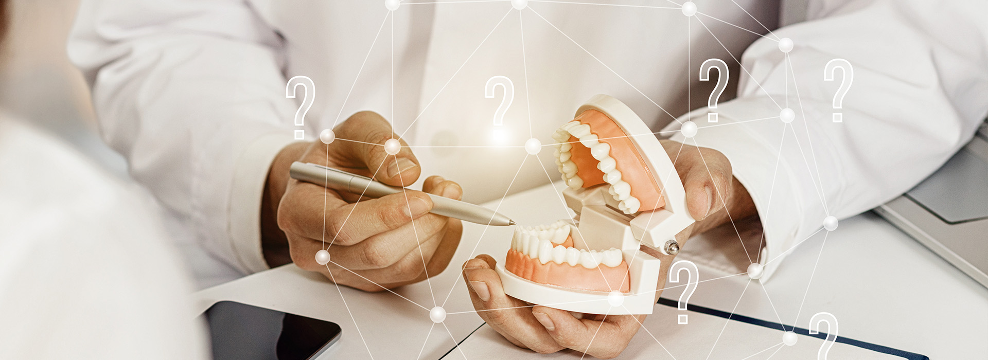 A person holding a model of a human tooth with various numbers and symbols around it, suggesting an educational or instructional context related to dental care or dental implants.