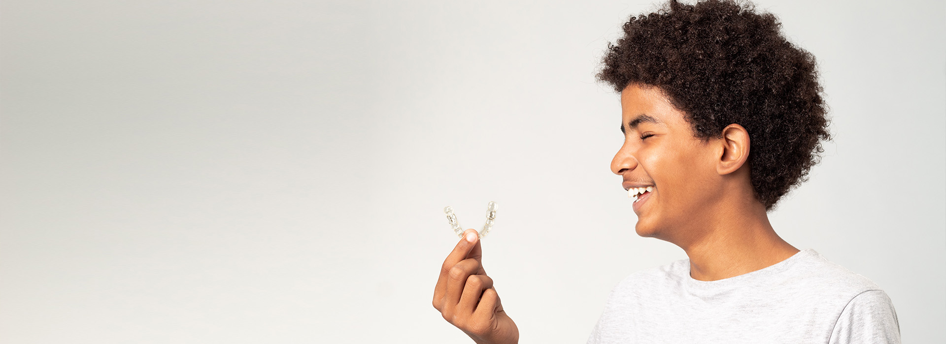 The image features a young person with an expressive smile holding a small object up to their face, set against a white background with a focus on the subject s joyful expression.