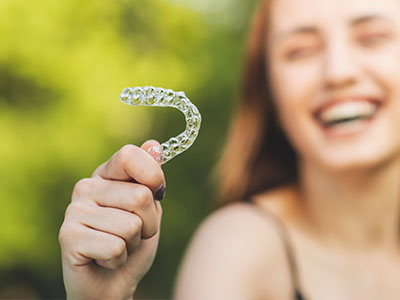 Woman holding a clear plastic toothbrush with a smile on her face.