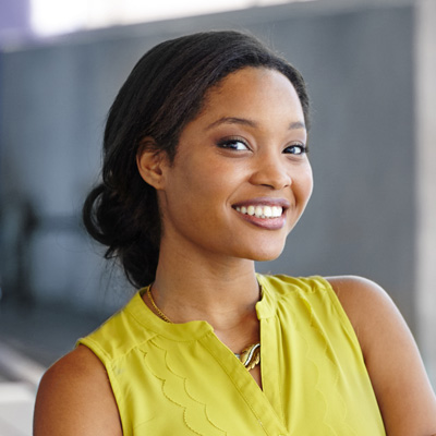 A smiling woman with short hair wearing a yellow top, posing against a backdrop.