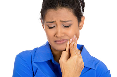 The image shows a woman with her mouth open, holding her finger near her teeth, seemingly examining them. She appears to be in a state of concern or discomfort.